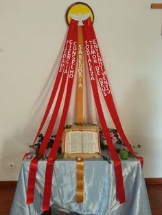 an open book on top of a table with red ribbon around it and a cross hanging from the ceiling