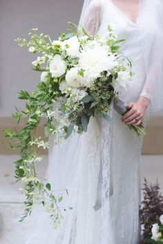 a bride holding a bouquet of white flowers and greenery on her wedding day at the church