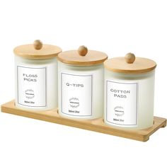 three white canisters with wooden lids on a wood tray, each containing two different labels