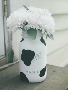 a mason jar with flowers in it sitting on a wooden table next to a house