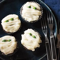 four cupcakes with white frosting on a plate next to a fork and knife