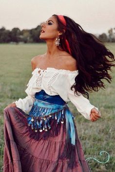 a woman with long hair wearing a skirt and white blouse in a field looking up at the sky