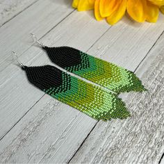 green and black seed beaded earrings sitting on top of a wooden table next to yellow flowers