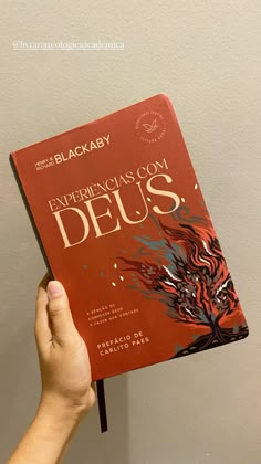 a person holding up a red book in front of a white wall with the words experience deus written on it