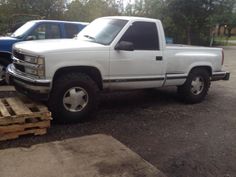 a white pick up truck parked in a parking lot next to pallets of wood