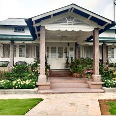 a white house with blue trim and flowers in the front yard