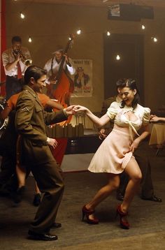 a man and woman dancing in an old - fashioned dance studio with other people around them