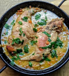 a skillet filled with meat and vegetables on top of a wooden table