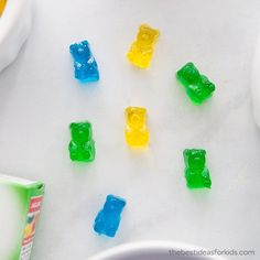 several gummy bears sitting on top of a white table next to a bowl of cereal