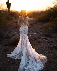 a woman standing in the desert at sunset wearing a wedding dress with long sleeves and an open back