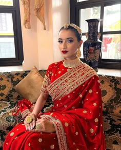 a woman in a red and gold sari sitting on a couch with her hand on her hip