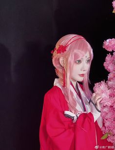 a woman with pink hair wearing a red kimono and standing next to some pink flowers