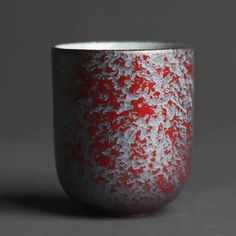 a red and white cup sitting on top of a gray table next to a black wall