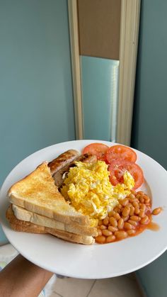 a plate with toast, beans and tomatoes on it is held up by someone's hand