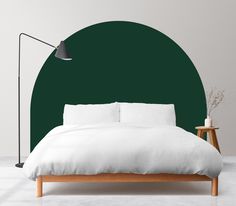 a bed with white sheets and pillows in front of a dark green circle wall behind it