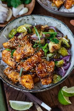 two bowls filled with chicken and vegetables on top of a wooden table next to chopsticks