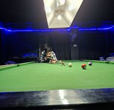 a man is playing pool in a dark room with blue lights on the ceiling and green felt