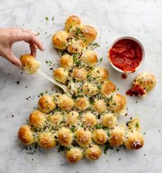 a christmas tree made out of rolls with sauce on the side and hands holding a spoon