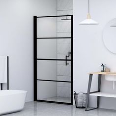 a white bathroom with a black frame and glass shower door in the corner, next to a bathtub