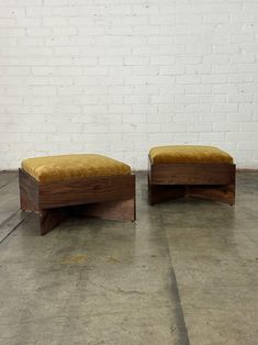 two wooden benches sitting next to each other on cement floored area with white brick wall