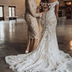 two women in wedding gowns standing next to each other with their hands on the dress