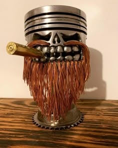 a metal skull with a long handle and fringes on it's head is sitting on a wooden table