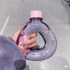 a person holding a pink and gray bottle with hearts on it's side, in front of a tile floor