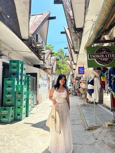 a woman in a white dress is walking down the street holding a shopping bag and looking at the camera