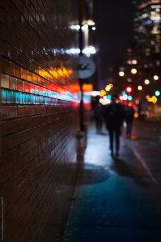 people walking down the sidewalk at night in the city by some buildings with lights on them