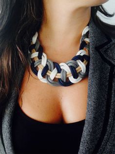 a close up of a woman wearing a black top and grey jacket with a multicolored necklace on her chest