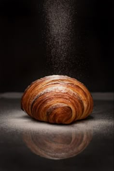 a piece of bread is being sprinkled with flour on a reflective surface, in front of a black background