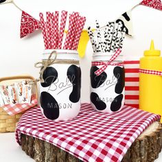 two painted mason jars sitting on top of a table with red and white checkered cloth