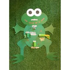 a paper cut out of a frog sitting on top of green grass with eyes and legs