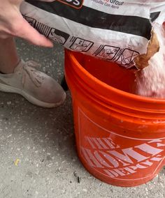 a person standing next to a red bucket filled with something white and black is pouring water into it