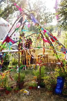 a tent that has been decorated with ribbons and streamers in the grass, surrounded by potted plants