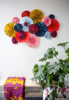 colorful paper fans are hanging on the wall above a wooden bench and potted plant