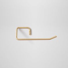 a gold metal hook on a white wall with the handle in the shape of a rectangle