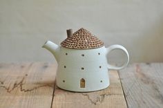 a ceramic teapot with a small house on the top is sitting on a wooden table