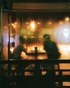 two people sitting at a table in front of a window with rain coming down on them