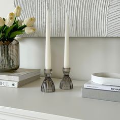 two candles are sitting on a table next to books and a vase with tulips