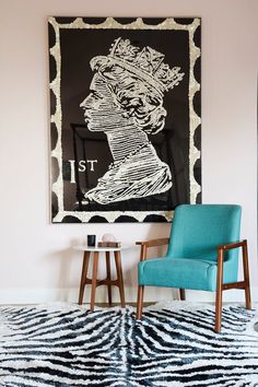 a blue chair sitting in front of a black and white painting on the wall next to a table