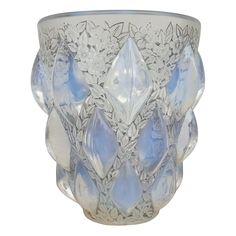 an ornate glass vase with blue flowers and leaves on the outside, in front of a white background