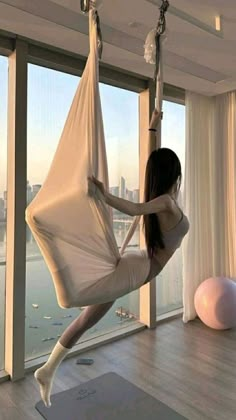 a woman is swinging on a hammock in front of a window with a city view