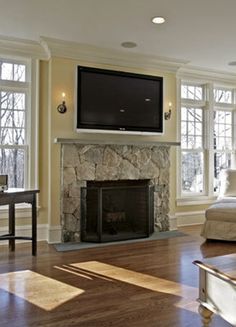 a living room with large windows and a television on the wall above it's fireplace