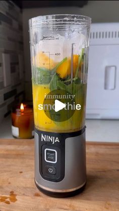 a blender filled with fruit and vegetables on top of a wooden counter next to a candle