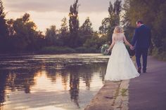 a bride and groom holding hands walking by the water