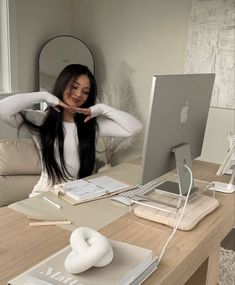 a woman sitting at a desk with her hands behind her head and looking at the computer screen