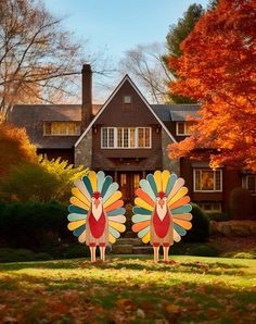 two large turkeys stand in front of a house with autumn leaves on the ground