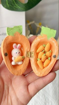 a hand holding two small carrots with a bunny figurine in the middle