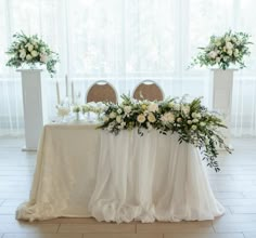 a table with white flowers and greenery is set up in front of two tall vases